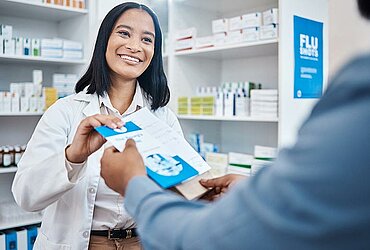 Freundliche Apothekerin überreicht einem Kunden einen Flyer