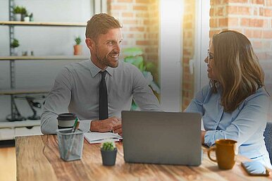 Zwei Geschäftsleute im Gespräch in einem modernen Büro, mit Laptop und Kaffeetassen auf dem Tisch