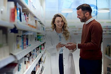 Apothekerin berät Kunden in einer Apotheke, während sie ein Medikament in den Händen hält