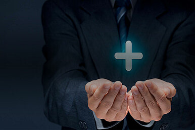 Geschäftsmann in Anzug hält leuchtendes Pluszeichen in den Händen, symbolisiert Wachstum und positive Entwicklung