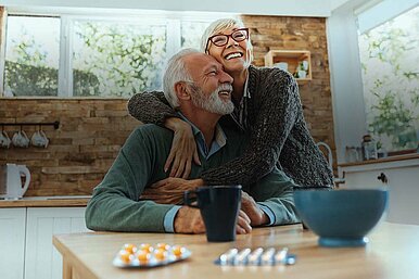 Glückliches älteres Paar lacht und umarmt sich liebevoll in moderner, sonniger Küche – Lebensfreude im Alter.