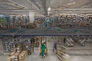 Großes Lagerhaus eines Pharmagroßhandels mit Regalen voller Kartons und Produkten, Förderbändern und Arbeitern